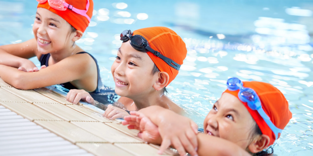 Three children in orange swim hats are in a swimming pool